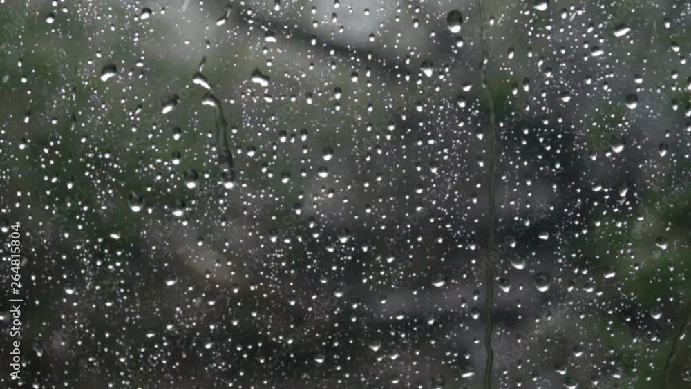 Rain on glass of window with green trees outside. Closeup. Slow motion. Rain on the glass. Rain drops water on car window background. Rain on glass of window with green trees outside. Closeup. Slow motion. Rain on the glass. Rain drops water on car window background.