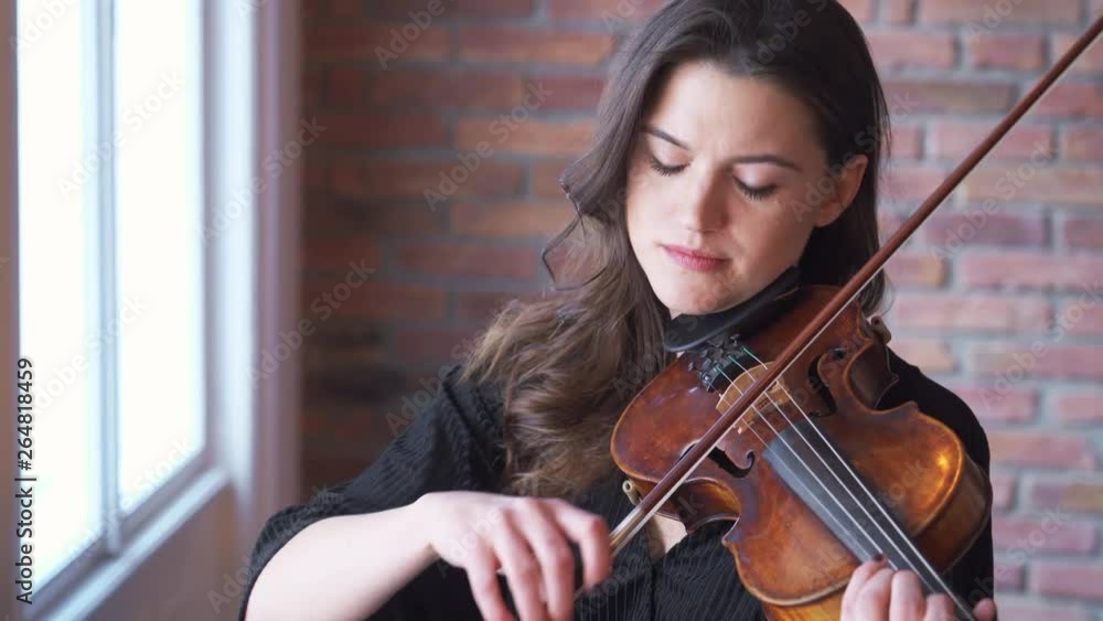 Close up of a pretty girl in an elegant black dress enjoying playing on her violin Close up of a pretty girl in an elegant black dress enjoying playing on her violin
