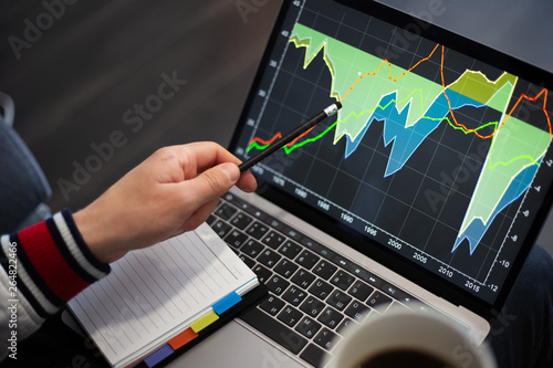 Young businessman analysing finance statistic on laptop with cup coffee in hand.