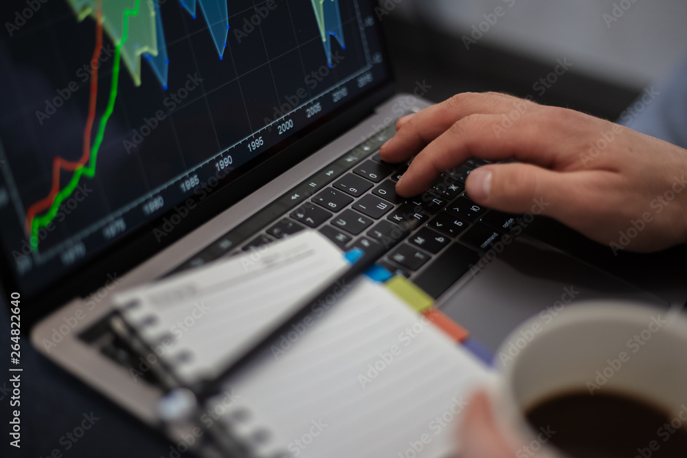 Close-up of man hands, typing on keyboard of laptop and holding mug of coffee, near notebook with black pencil. Close-up of man hands, typing on keyboard of laptop and holding mug of coffee, near notebook with black pencil.