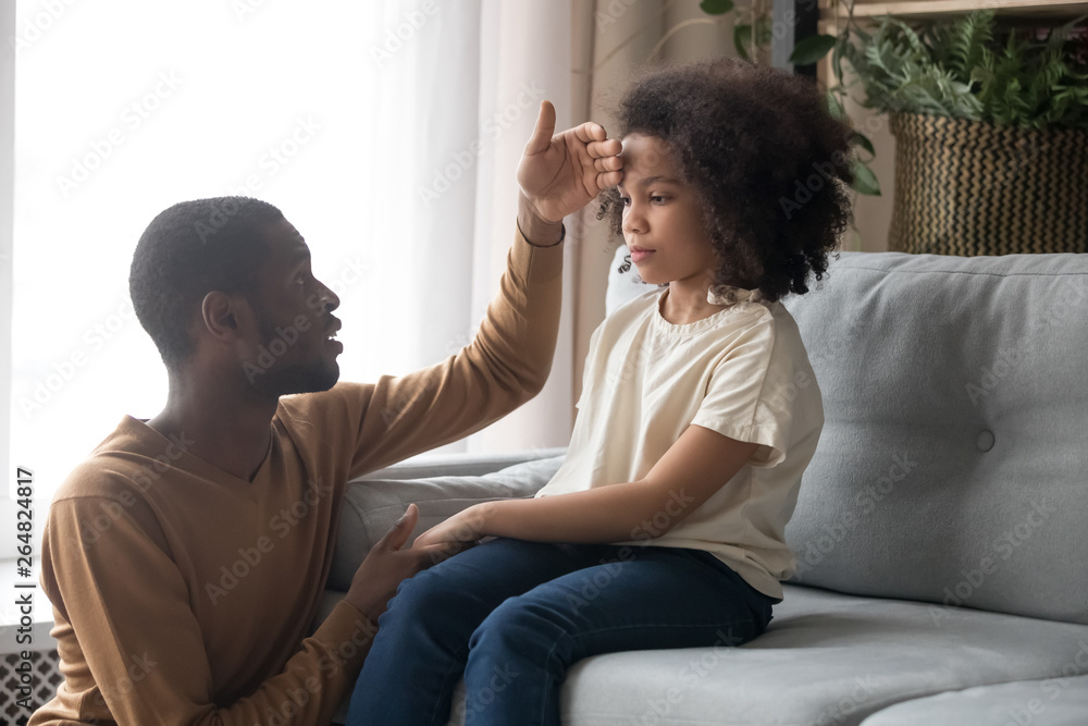 Worried father touch forehead of unhealthy daughter sitting on sofa Worried father touch forehead of unhealthy daughter sitting on sofa