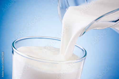 Pouring fresh milk into glass from jug on a blue background