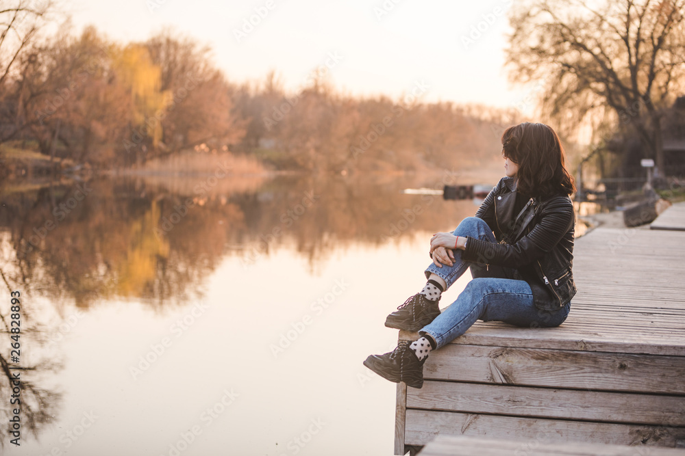 young pretty fashion woman sitting on pier on sunset with beautiful view of river young pretty fashion woman sitting on pier on sunset with beautiful view of river