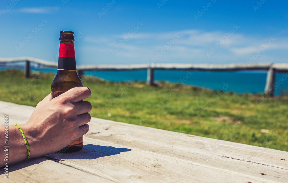 Male hand holding bottle of beer on the sea beach on the wooden platform Male hand holding bottle of beer on the sea beach on the wooden platform