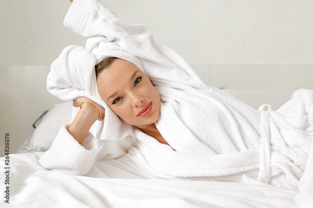 A young girl with white hair in her bedroom is posing on a bed in a white coat and a white towel on her head. A young girl with white hair in her bedroom is posing on a bed in a white coat and a white towel on her head.