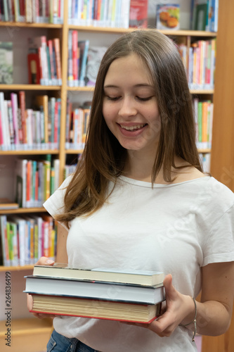 Portrait of a smiling student girl standing holding books in the school library