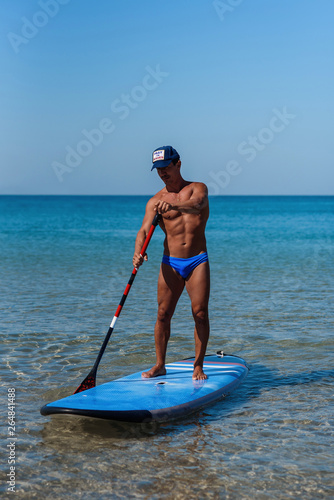 Sporty healthy person stands on his surfboard on the water, and rowing by oar. The concept of sporty and healthy lifestyle.