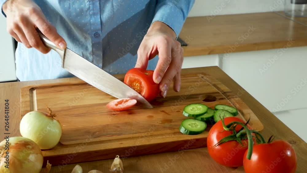A young woman who is cooking and cutting fresh tomatoes for salad on cutting board A young woman who is cooking and cutting fresh tomatoes for salad on cutting board