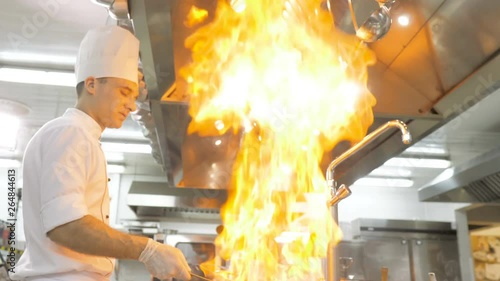 Chefs cooks and doing flambe on vegetables in pan in restaurant kitchen