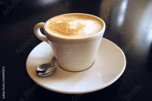 A mug of cappuccino on a saucer stands on a dark table macro photo for design.