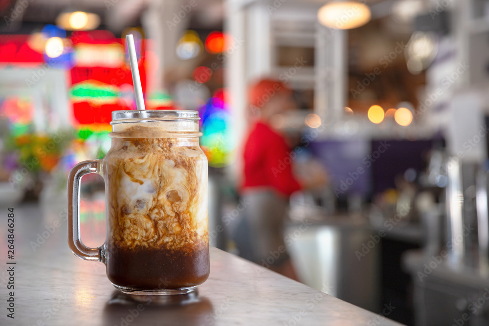 Freshly served iced latte coffee drink in a jar, on cafe diner counter, with mocha syrup cream swirl