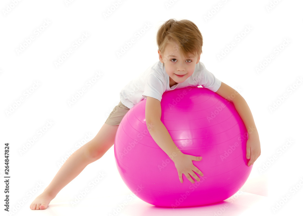The little boy on the big ball is engaged in fitness. White T-sh The little boy on the big ball is engaged in fitness. White T-sh