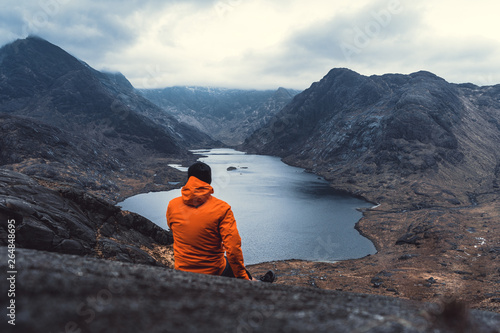  Young man sitting on rock looking out over Loch Coruisk Lake and the Cuillin Mountains. Listening to the Silence. Beautiful moment the miracle of nature. photo