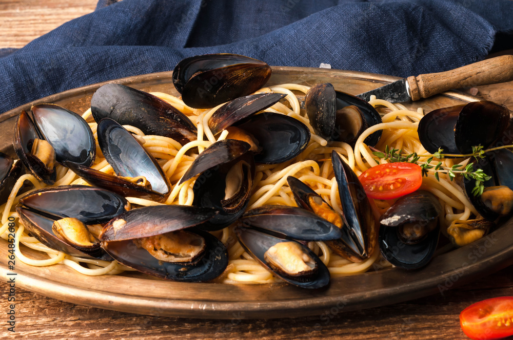 delicious mussels in shells cooked in sauce with pasta and tomatoes on golden metal plate with blue cloth on wooden background delicious mussels in shells cooked in sauce with pasta and tomatoes on golden metal plate with blue cloth on wooden background
