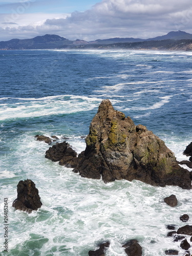 The rugged cliffs at Yaquina Head with the blue waters of the Pacific Ocean crashing into them on the Central Oregon Coast on a sunny spring day.