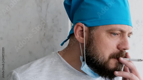 Funny doctor after a difficult operation removes the mask and begins to nervously smoke. Close up photo