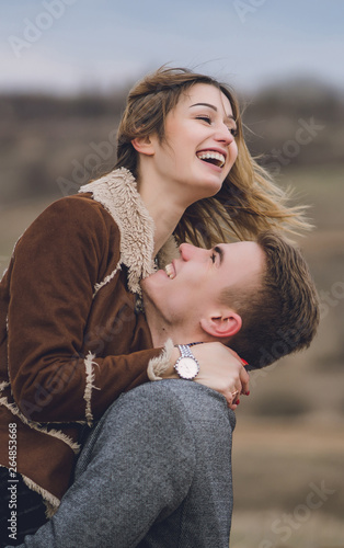 beautiful lovely couple in the park or field or track. man in coat and scarf with girl in coat. man hugs picked women up flirting laugh and look at each other. emotional soulful photo vertical