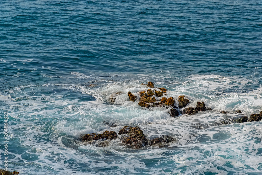 Beautiful view of clear turquoise mediterranean sea waves crash on rocks at wild rocky shore. Blanes, Costa Brava, Spain.