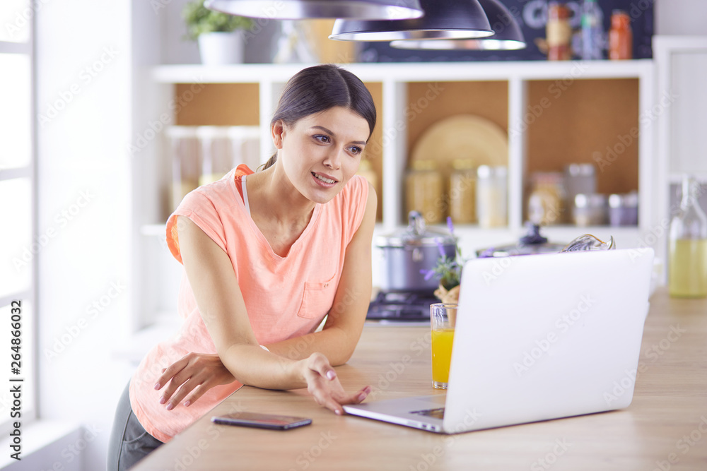 Pretty woman on the phone using laptop at home in the kitchen Pretty woman on the phone using laptop at home in the kitchen