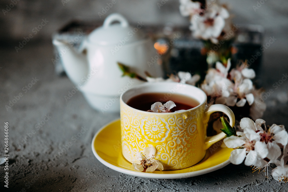 Fototapeta premium Tea served in a yellow teacup and saucer decorated with spring flowers