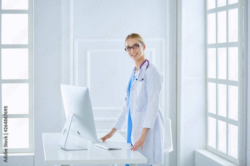 Young doctor woman standing near table, isolated on white background