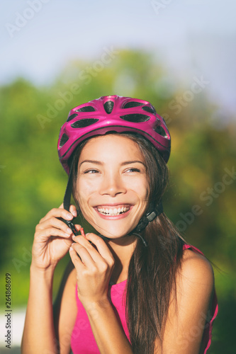 Biking safety - Asian woman putting on pink fashion bike helmet for commute to work-city cyclist . Active summer sport lifestyle.