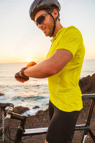 Smartwatch biking athlete man cyclist on triathlon race using smart watch on road bike insunset summer outdoor. photo