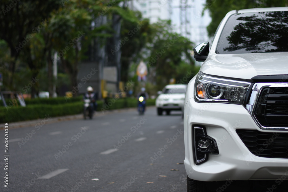 Focusing on the White car headlights on a street corner with sunlight flares, In the background, the driver, bike and car. Car parking on the street.  space for insert text.