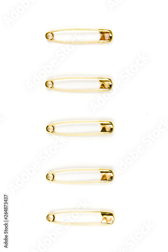 Five gold safety pins individually stacked on a white background