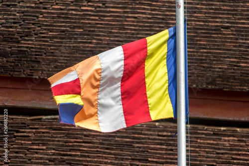 Flying Standard' Buddhist Flag on the background of the roof in Buddhist temple. The Vat Phramahathat Rajbovoravihane temple in Luang Prabang, Laos. photo