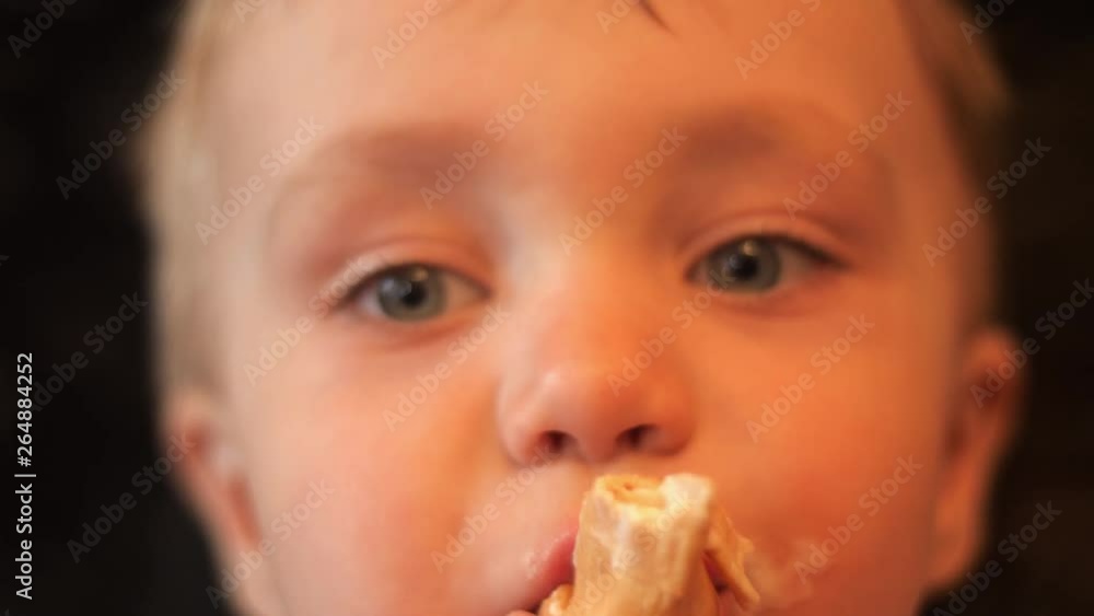 an adorable baby boy eating the waffle cup of vanilla ice cream and the kid looks into camera and around himself in slow motion portrait close up 4K video. an adorable baby boy eating the waffle cup of vanilla ice cream and the kid looks into camera and around himself in slow motion portrait close up 4K video.