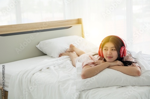 Portait of smiling lady in pink pajama wake up listening to music with headphone on the bed
