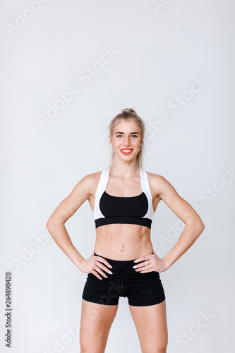 Portrait of fit and sporty young woman doing stretching on gray.