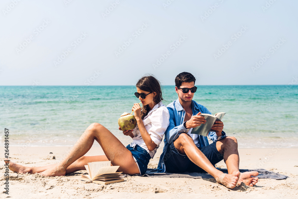 Young couple drinking coconut juice and reading a book on the tropical beach.Couple relaxing on the beach.Summer vacations Young couple drinking coconut juice and reading a book on the tropical beach.Couple relaxing on the beach.Summer vacations