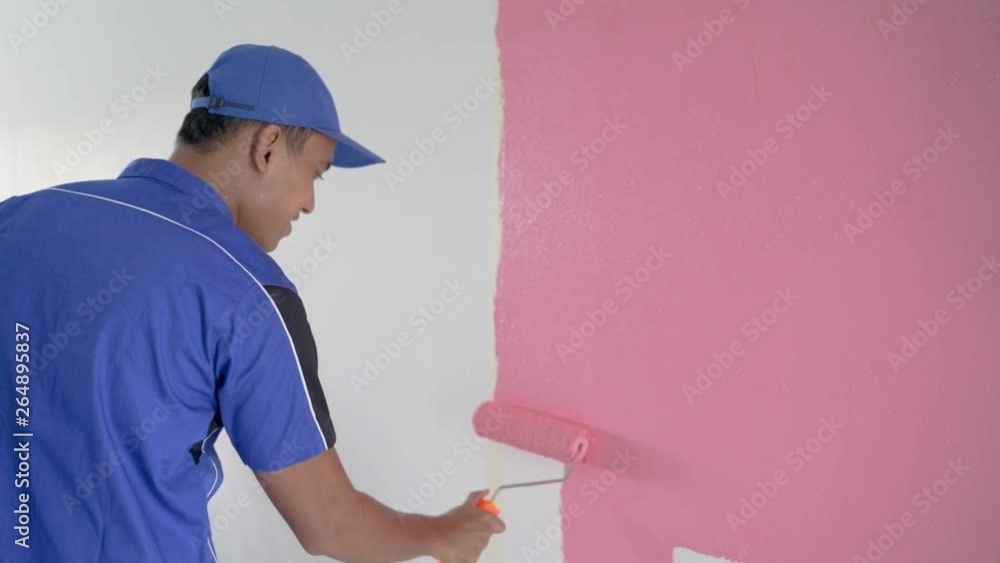 worker with blue uniform painting on the wall room with pink color