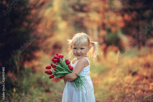 Little beautiful girl smiling with tails on her head in white dress with a bouquet of tulips