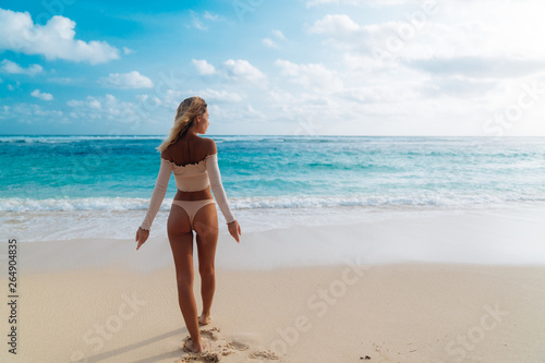 Backside view of girl with sexy booty in pink bikini resting on deserted beach