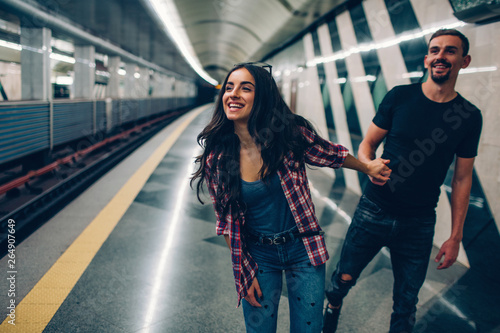 Young man and woman use underground. Couple in subway. Young woman hold man in hand. He follow her. Young woman smiles. Fast train moves. Action. Love story.