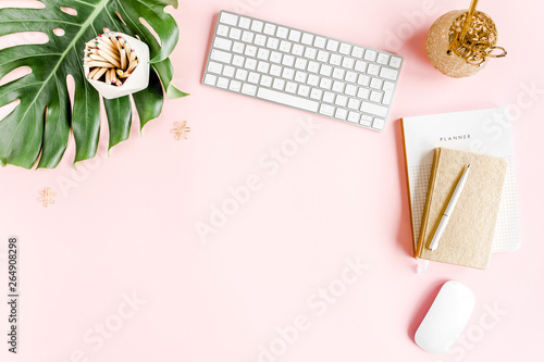 Flat lay home office desk. Female workspace with computer   tropical palm leaves  Monstera  accessories on pink background. Top view feminine background. 