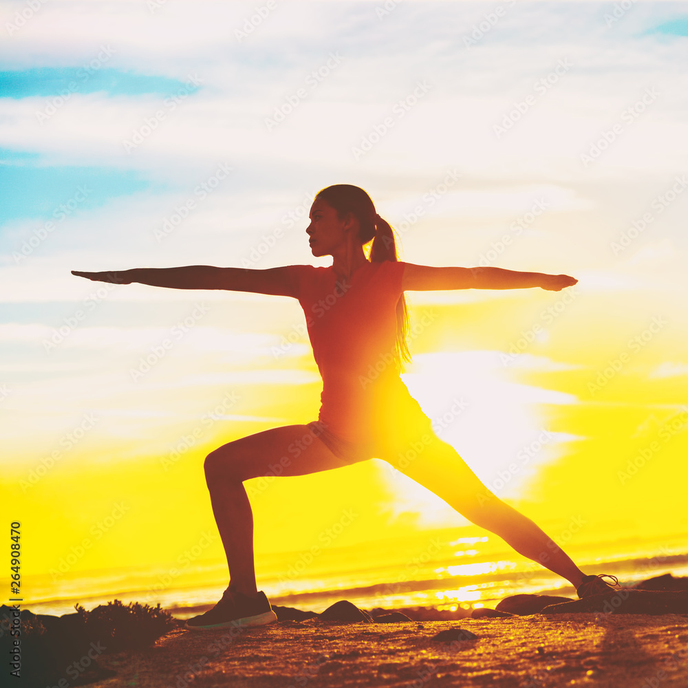 Woman doing yoga on beach. Fit girl in Warrior II pose standing in silhouette against sun flare background. Square crop for social media.