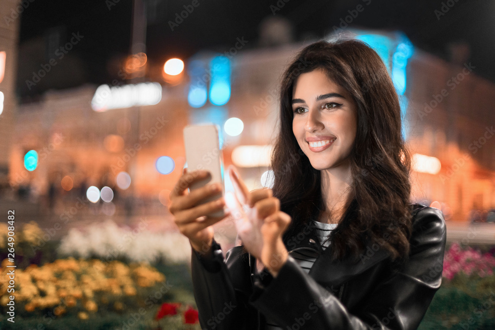 Woman checking social networks, walking in night city