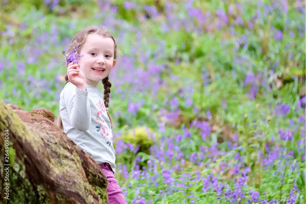 Young girl happy laughing picking bluebell flowers outside in spring summer forest woodland