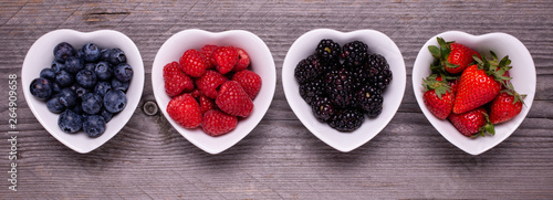 in the four white ceramic heart-shaped bowls, ripe berries, in the foreground, on the rough wooden table photo