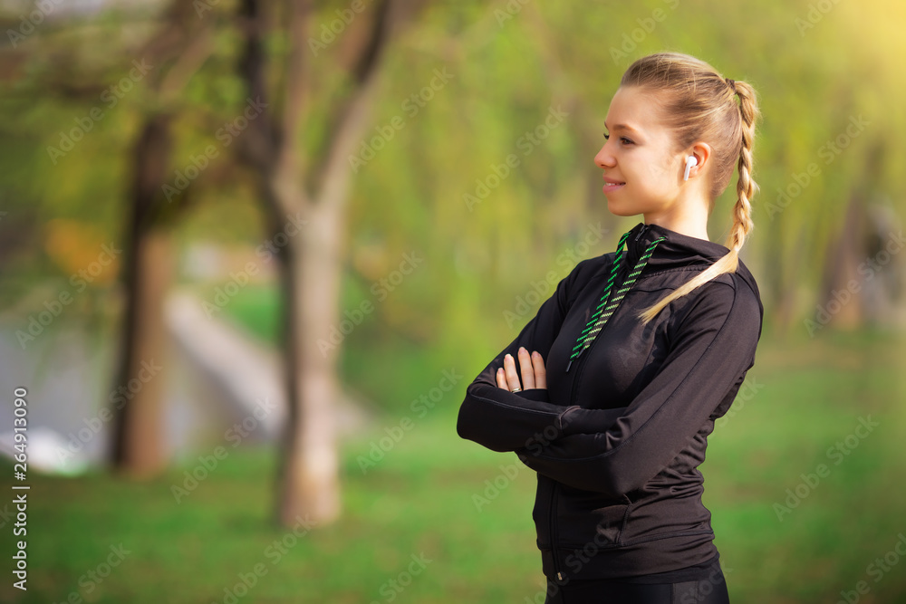 Beautiful young woman trainer standing on the park running with cross hands and looking at the camera inviting to sport and listening to music with wireless headphones - motivation health photo Beautiful young woman trainer standing on the park running with cross hands and looking at the camera inviting to sport and listening to music with wireless headphones - motivation health photo