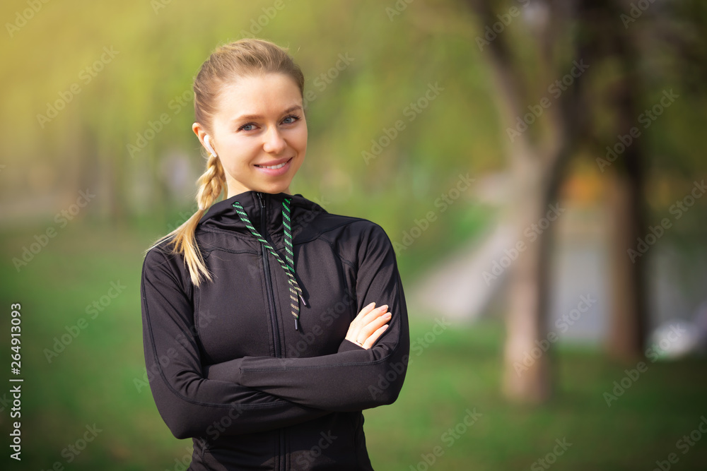 Beautiful young woman trainer standing on the park running with cross hands and looking at the camera inviting to sport and listening to music with wireless headphones - motivation health photo Beautiful young woman trainer standing on the park running with cross hands and looking at the camera inviting to sport and listening to music with wireless headphones - motivation health photo