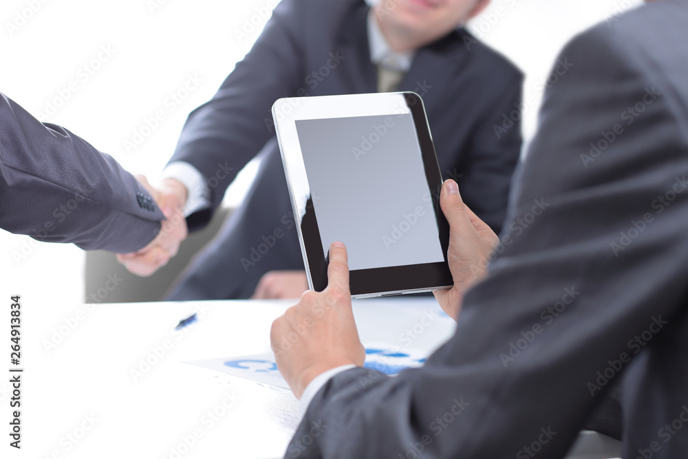 businessman with a digital tablet on the background of a handshake of business partners businessman with a digital tablet on the background of a handshake of business partners
