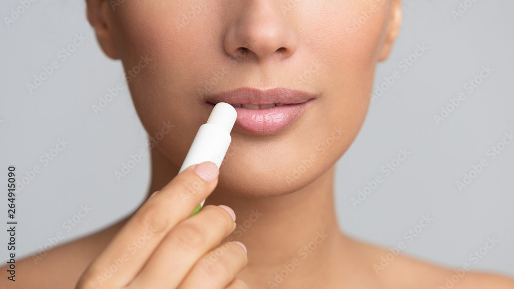 Girl applying hygienic lip balm on grey background Girl applying hygienic lip balm on grey background