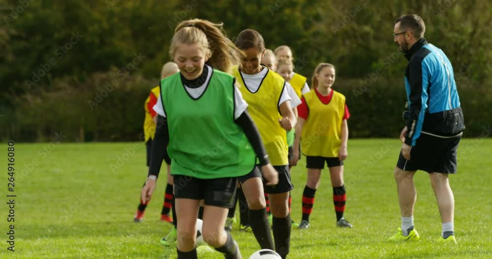 4K Happy teen girls smiling, having fun at soccer training with sports coach. Slow motion.