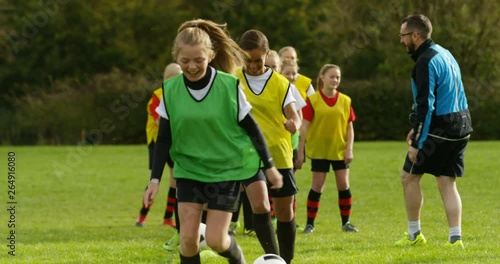 4K Happy teen girls smiling, having fun at soccer training with sports coach. Slow motion.