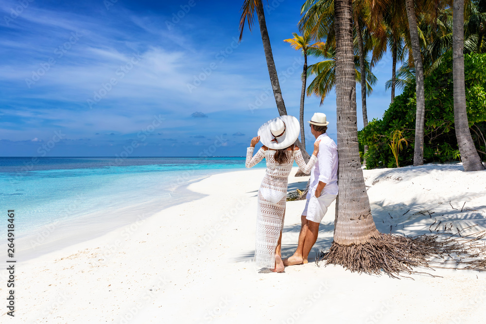 Glückliches Paar steht an einem tropischen Strand unter Palmen und genießt den Urlaub
